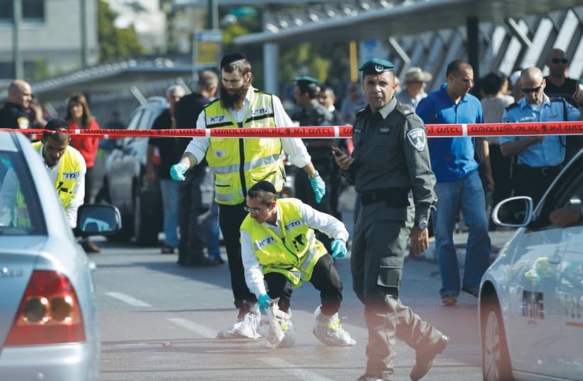 ZAKA SEARCH AND RECOVERY organization members and a border policeman work at the scene of yesterday’s attack near the Hagana train station in south Tel Aviv (photo credit: REUTERS)