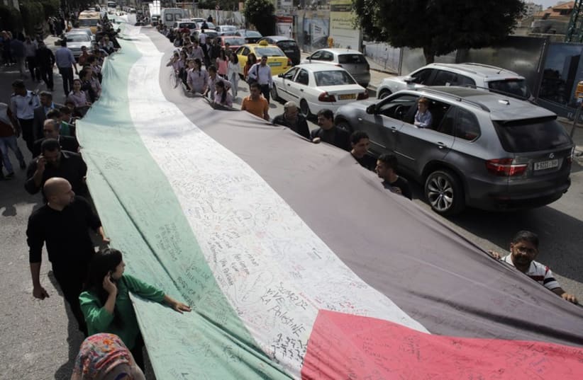 PEOPLE MARCH as they hold a large Palestinian flag in Ramallah in October (photo credit: REUTERS)