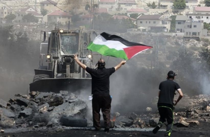 A protester holds a Palestinian flag in front of an IDF bulldozer in the West Bank [File] (photo credit: REUTERS)