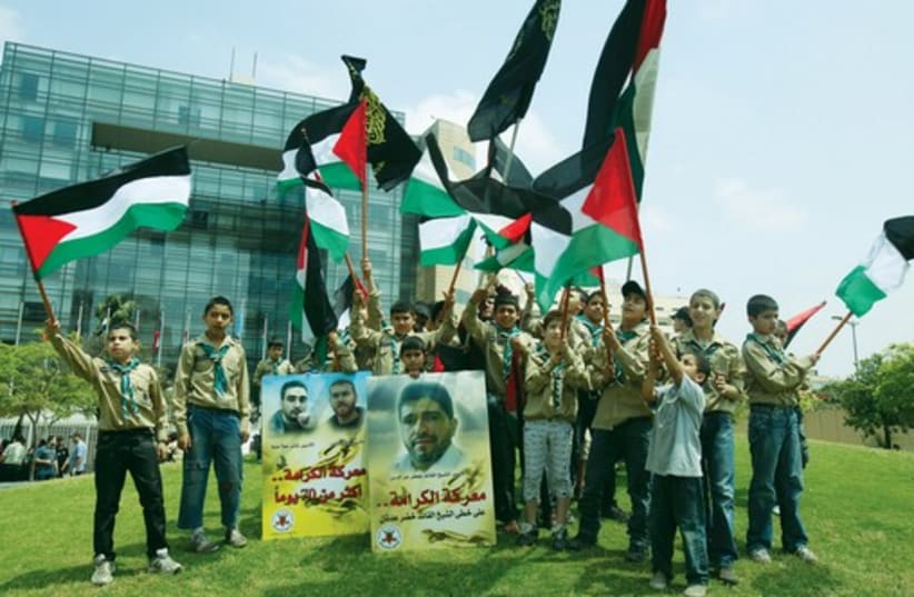 Palestinian members of a youth group wave their national flags and hold posters depicting portraits of Palestinian prisoners during a protest in solidarity with them. (photo credit: REUTERS)