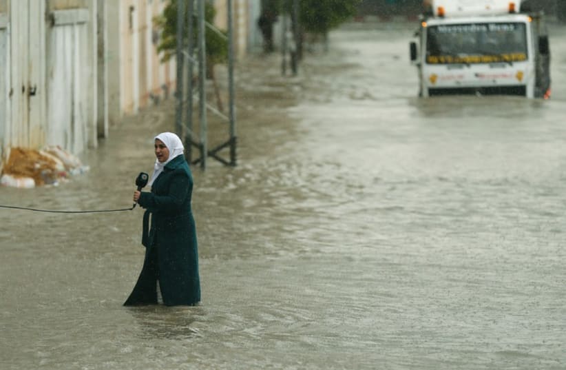A Palestinian journalist speaks to the camera as she stands on a flooded street, (photo credit: REUTERS)