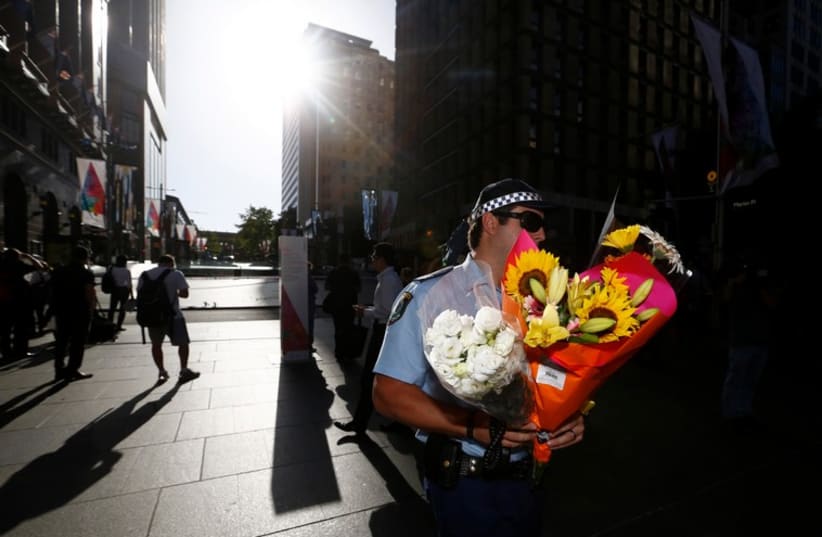 An Australian police officer carries a bouquet left as a floral tribute after the Sydney cafe siege ended December 16, 2014.  (photo credit: REUTERS)