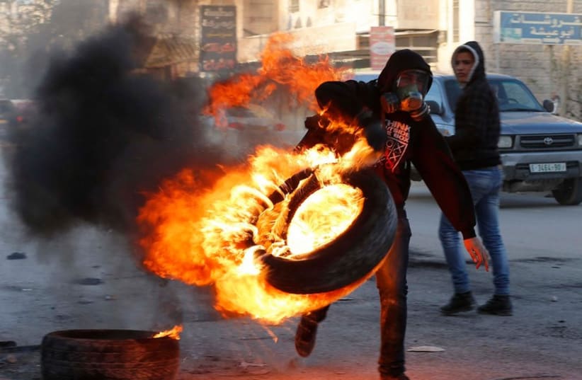 A Palestinian carries a burning tire during clashes with Israeli troops following the funeral of Palestinian Mahmoud Adwan at Qalandia checkpoint near the West Bank city of Ramallah (photo credit: REUTERS)