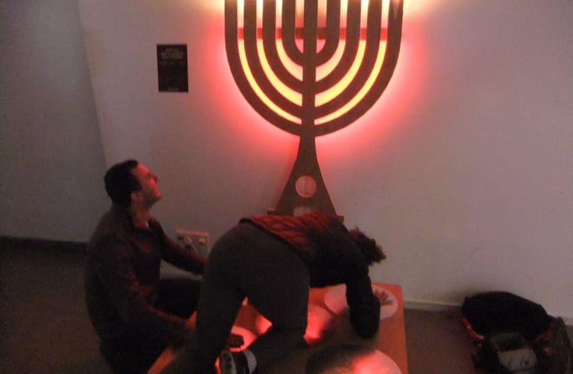 Adults play with a hanukkia that lights up when limbs used to make an electrical circuit.  (photo credit: JUDY SIEGEL-ITZKOVICH)