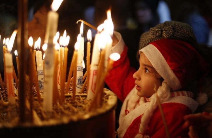 A child dressed as Santa Claus lights a candle in the Church of the Nativity in Bethlehem (photo credit: REUTERS)