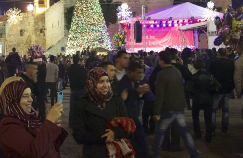  A large illuminated Christmas stands high over the crowd in Manger Square, Bethlehem on Christmas eve, which is buttressed by the the Church of Nativity and the Mosque of Omar. (photo credit: DOV LIEBER)