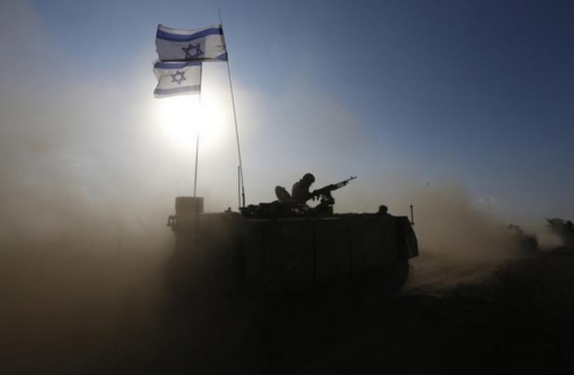 An IDF soldier rides an armored personnel carrier toward a staging area near the Gaza border (photo credit: REUTERS)
