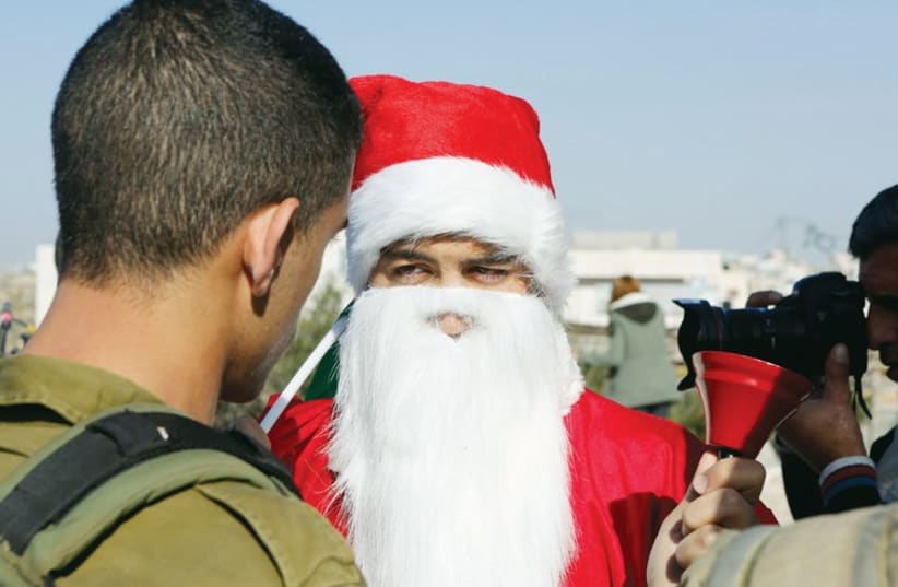 A Palestinian protester dressed in a Santa Claus costume rings a bell as he argues with an Israeli soldier during a protest near Bethlehem (photo credit: REUTERS)