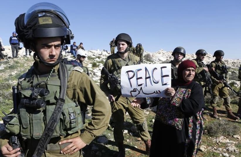 A protester holds a placard as she stands next to Israeli soldiers during a protest against Israeli settlements in Beit Fajjar town south of the West Bank city of Bethlehem (photo credit: REUTERS)