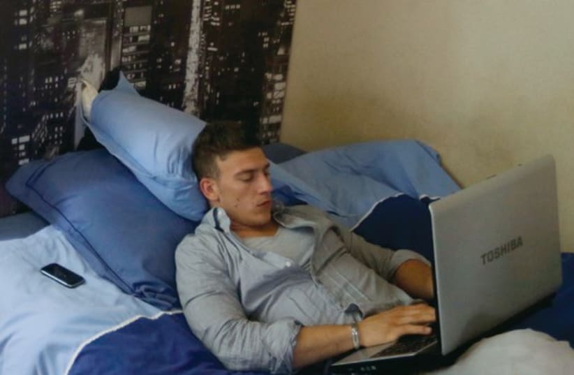 A young man works from his laptop in his bedroom of his mother’s home in France. (photo credit: ILLUSTRATIVE: REUTERS)