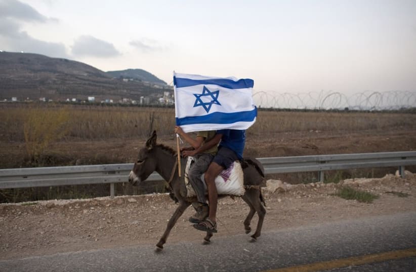 Jewish youths hold an Israeli flag as they ride a donkey during a rally march outside the West Bank settlement of Itamar, near Nablus (photo credit: REUTERS)