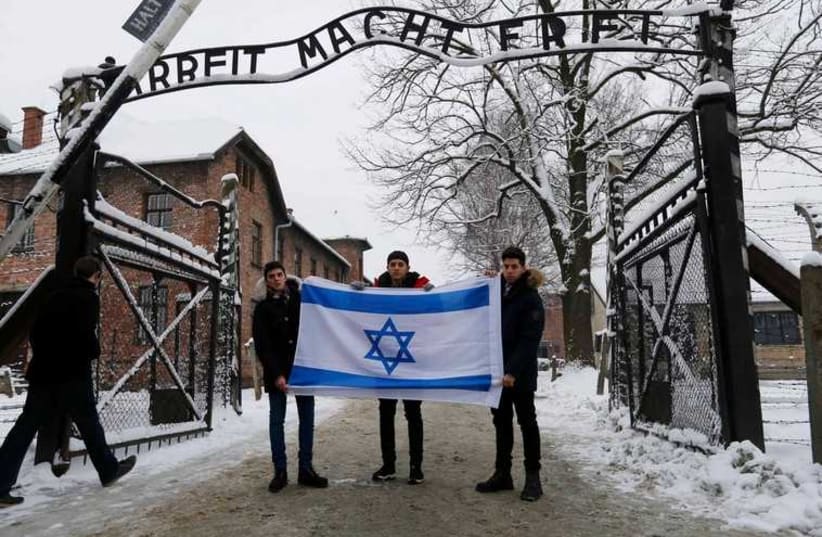 A group of visitors hold an Israeli flag in front of the gate of the former Nazi death camp of Auschwitz, January 26 (photo credit: REPRODUCTION)