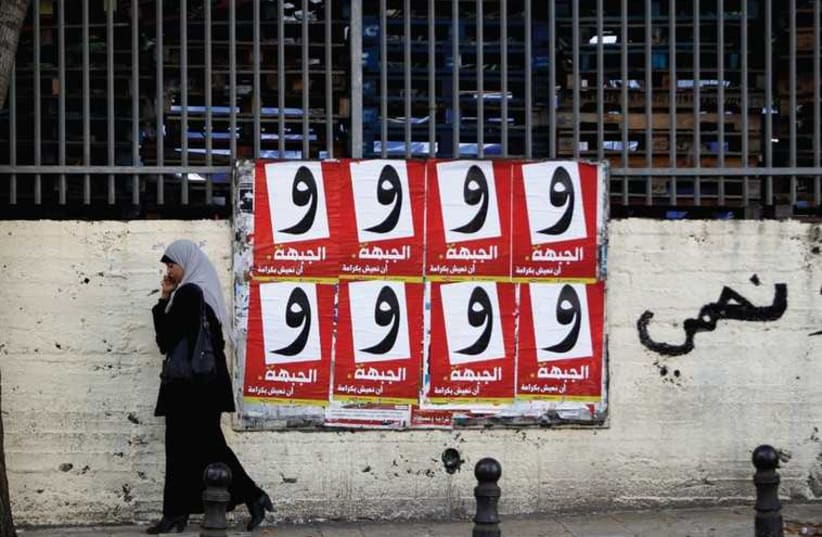 A WOMAN walks past campaign posters for the Arab-led Hadash party in the Israeli-Arab city of Umm al-Fahm (photo credit: REUTERS)