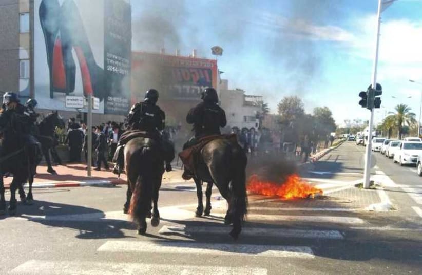 Police officers on horseback face Haredi protestors in Ashdod as a fire burns on the street (photo credit: ISRAEL POLICE)