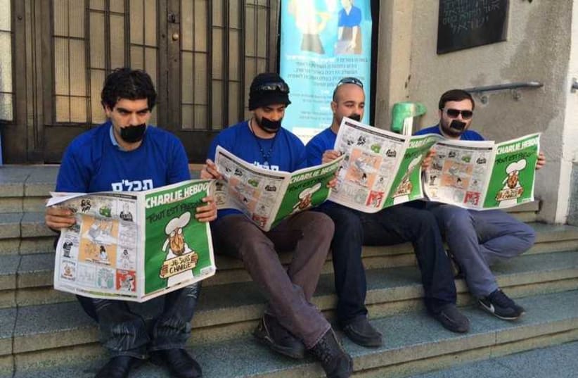 Yisrael Beytenu activists reading Charlie Hebdo with their mouths taped shut in front of Independence Hall in Tel Aviv (photo credit: Lahav Harkov)