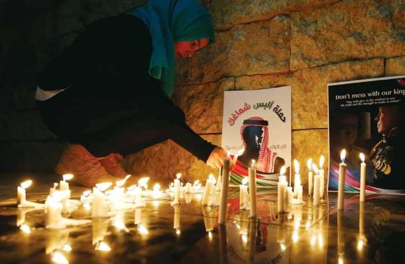 A woman lights a candle near a poster of Jordan’s King Abdullah II (photo credit: REUTERS)