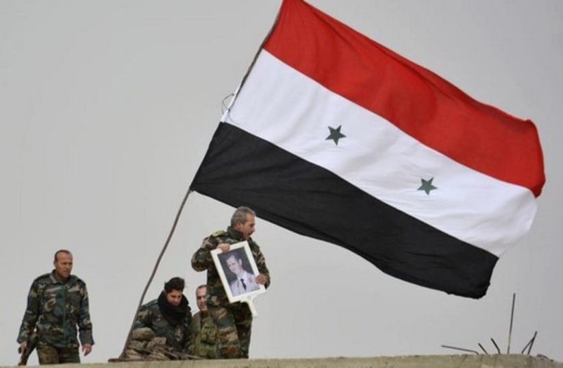 A fighter loyal to Syria's president Bashar Assad holds his picture as fellow fighters rest by a Syrian national flag after gaining control of the area in Deir al-Adas, a town south of Damascus (photo credit: REUTERS)