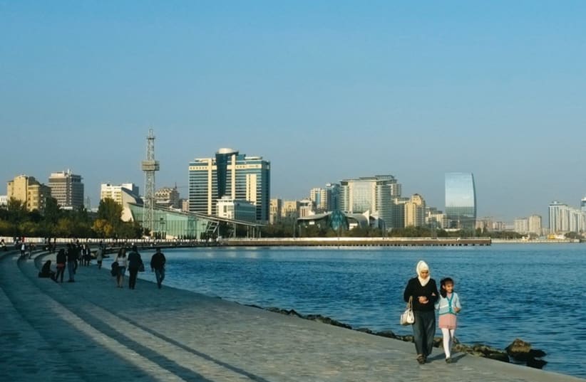 People walk along a seafront, with high-rise residential and commercial buildings in the background, in Baku on October 13, 2013. (photo credit: REUTERS)