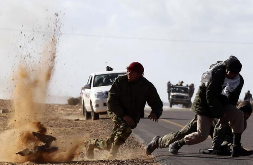 Rebel fighters jump away from shrapnel during heavy shelling by forces loyal to Libyan leader Muammar Gaddafi near Bin Jawad in this March 6, 2011 file photo (photo credit: REUTERS)