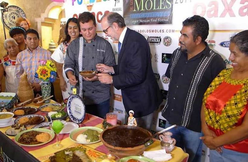 Chef Jose Cepeda Gonzalez (left) holds out a plate of goat mole to the Mexican consul in Los Angeles, Carlos Manuel Sada. (photo credit: YAKIR LEVY)
