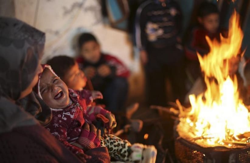 Members of a Palestinian family warm themselves by a fire at the remains of their house that witnesses said was destroyed by Israeli shelling (photo credit: REUTERS)