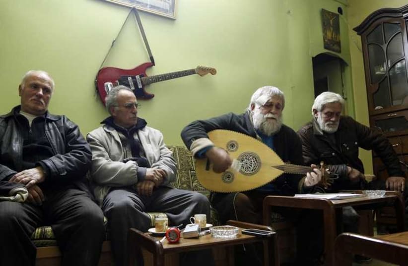 Ibrahim Dawoud (2nd R) plays music on an Oud next to his brother (R) and neighbors inside their home in the ancient Christian quarter of Bab-Touma in Damascus  (photo credit: REUTERS)