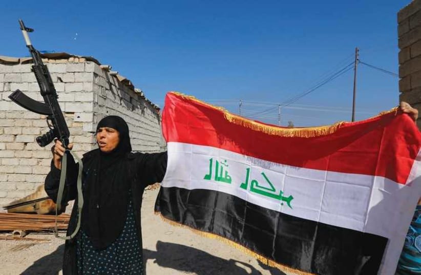 A WOMAN raises a weapon and the Iraqi flag in celebration after Iraqi government troops and militias drove Islamic State insurgents out of the town of al-Alam on Tuesday, clearing a final hurdle for an assault on the city of Tikrit. The Arabic characterson the flag read, ‘God is the greatest.’ (photo credit: REUTERS)