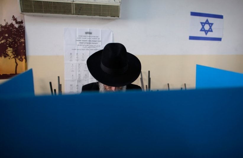 A ultra-Orthodox Jewish man stands behind a voting booth at a polling station  (photo credit: REUTERS)