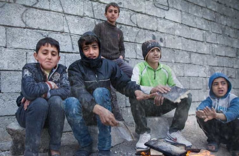 Assyrian Christian children who were displaced by the Islamic State terror group are pictured in Ankawa, Iraq, trying to keep warm during a snowstorm (photo credit: JNS.ORG)