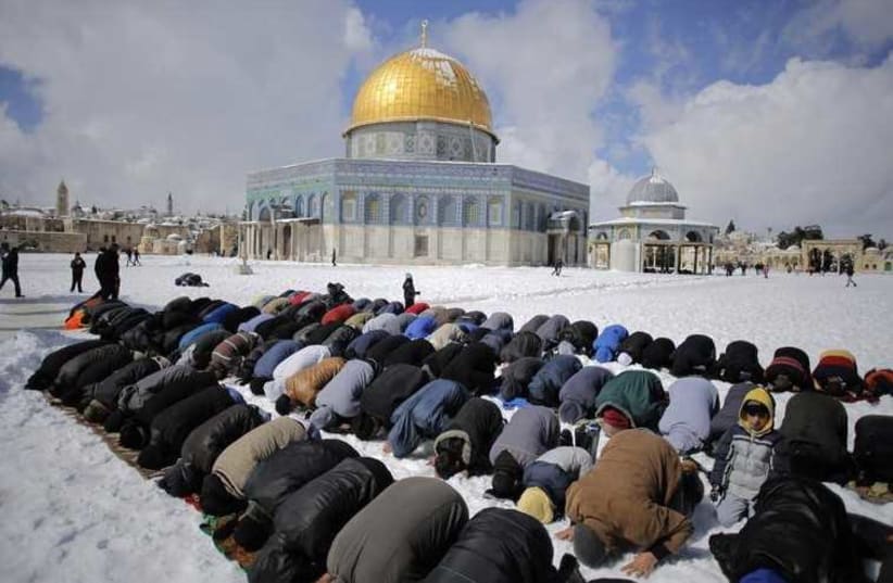 Palestinian men pray in front of the snow-covered Dome of the Rock in Jerusalem's Old City (photo credit: REUTERS)