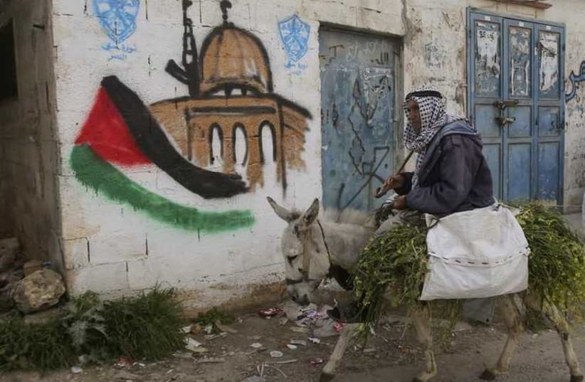 A Palestinian villager rides his donkey past a mural in the West Bank village of Awarta near Nablus (photo credit: REUTERS)