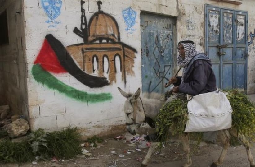 A Palestinian villager rides his donkey past a mural in the West Bank village of Awarta near Nablus (photo credit: REUTERS)
