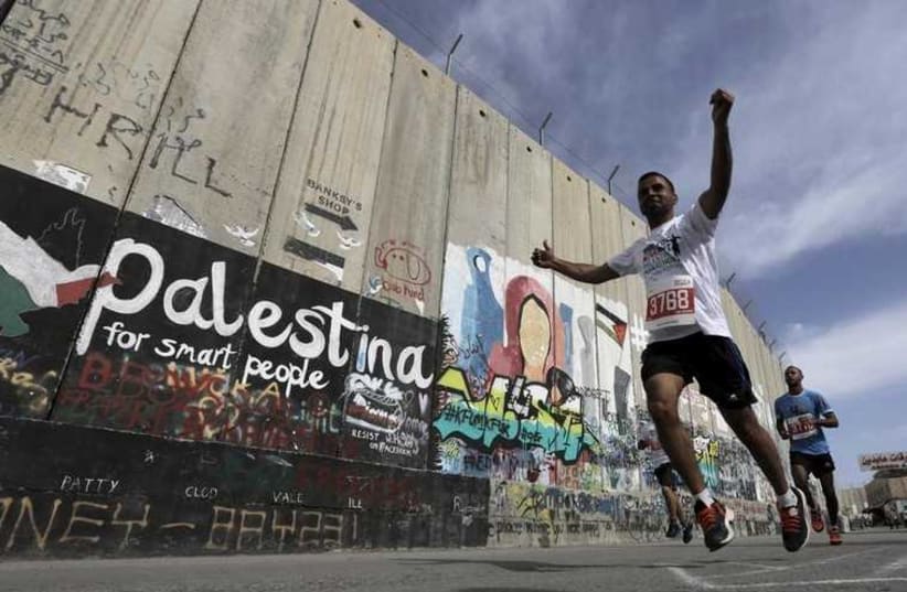 Participants run past the controversial Israeli barrier during the Palestine Marathon in the West Bank town of Bethlehem (photo credit: REUTERS)