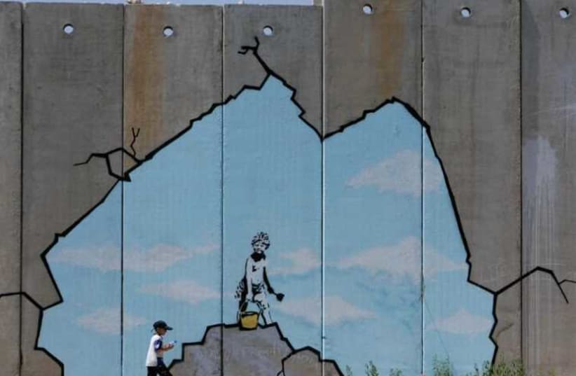 A Palestinian boy walks past a drawing by British graffiti artist Banksy (photo credit: REUTERS)
