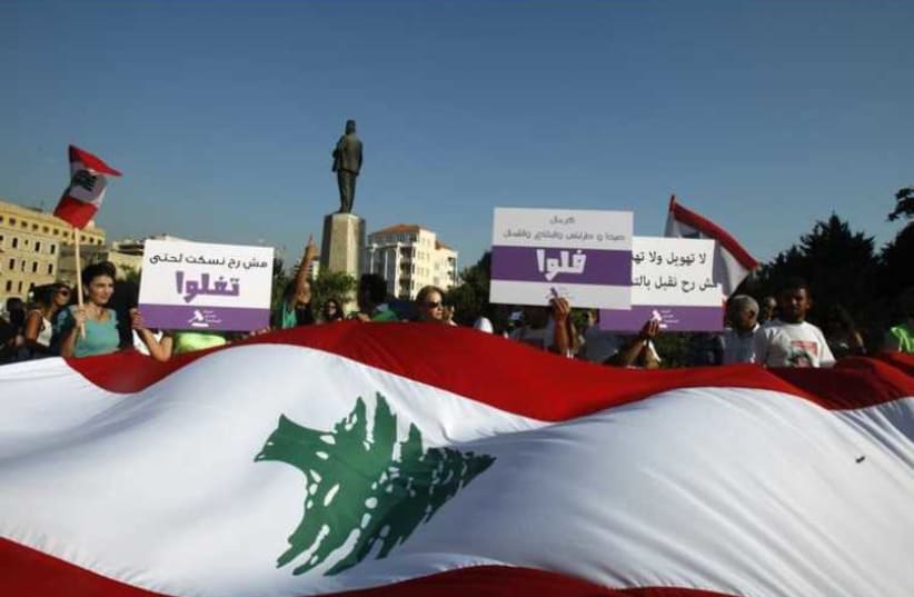 Activists and members of civil society organizations hold placards as they carry a giant Lebanese flag during a protest against the extension of the parliament terms (photo credit: REUTERS)