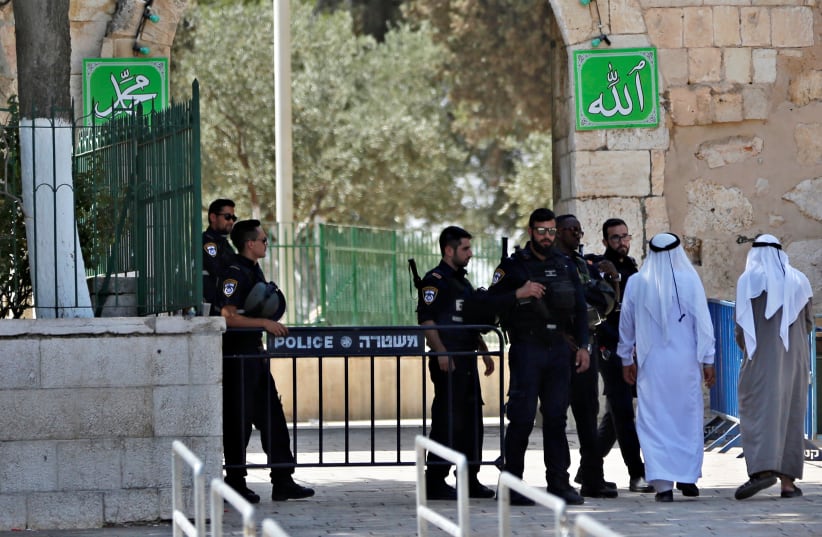 Palestinians walk next to Israeli security forces at the entrance of the compound known to Muslims as Noble Sanctuary and to Jews as Temple Mount at morning after Israel removed the new security measures there, in Jerusalem's Old City (photo credit: RONEN ZVULUN/REUTERS)