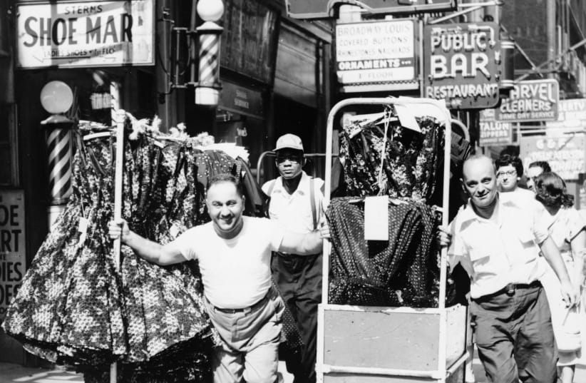 Men pulling racks of clothing on busy sidewalk in Garment District, New York City, 1955 (photo credit: PUBLIC DOMAIN / AL RAVENNA - WORLD TELEGRAM STAFF PHOTOGRAPHER)