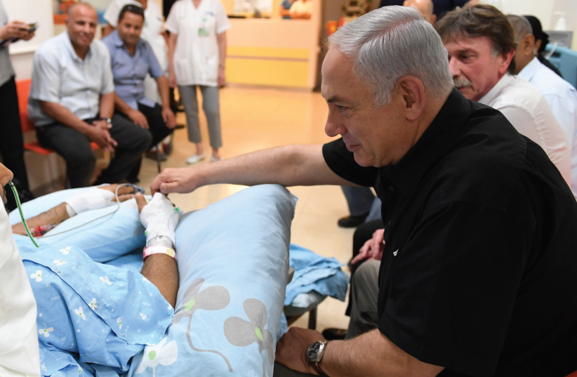Prime Minister Benjamin Netanyahu visits Niv Nehemiah yesterday at Kaplan Medical Center in Rehovot. Nehemiah was stabbed last week by a terrorist at a supermarket in Yavne. (photo credit: KOBI GIDEON/GPO)