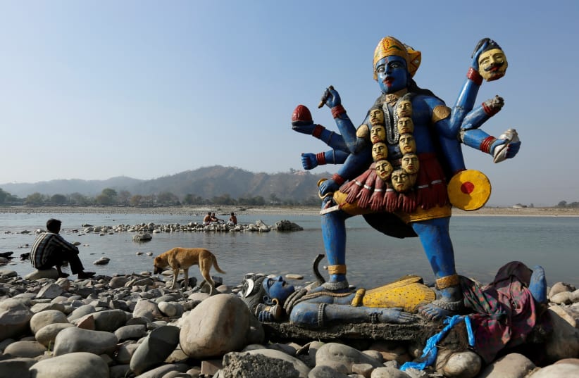 A man sits next to a damaged idol of Hindu goddess Kali which was taken out after its immersion in the river Ganges in Haridwar, India, March 29, 2017.  (photo credit: DANISH SIDDIQUI/ REUTERS)