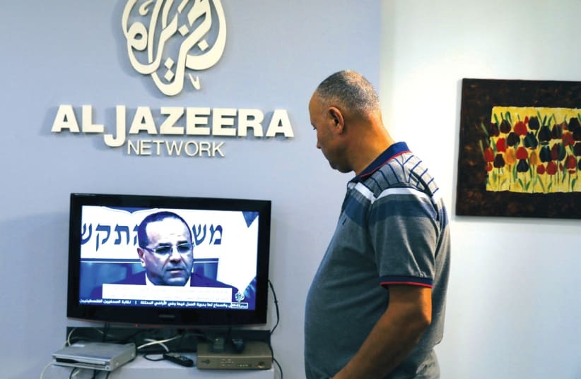 AN EMPLOYEE working inside the office of Qatar-based Al- Jazeera network in Jerusalem watches the news, last month. (photo credit: AMMAR AWAD / REUTERS)