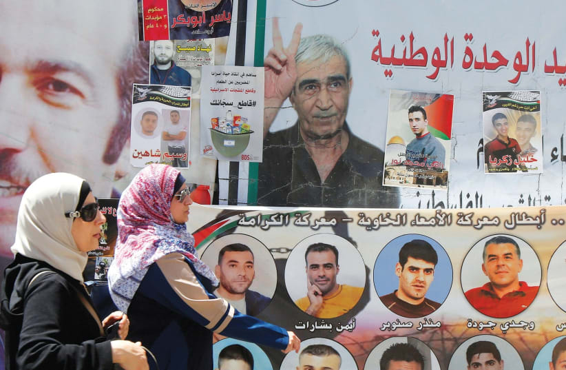 WOMEN WALK past pictures of Palestinian prisoners on hunger strike in Israeli jails, in Nablus in May (photo credit: REUTERS)