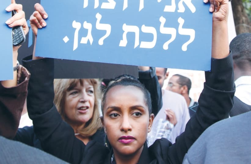 An Ethiopian woman holds a sign that says "Mom, I want to go to kindergarten." (photo credit: MARC ISRAEL SELLEM/THE JERUSALEM POST)