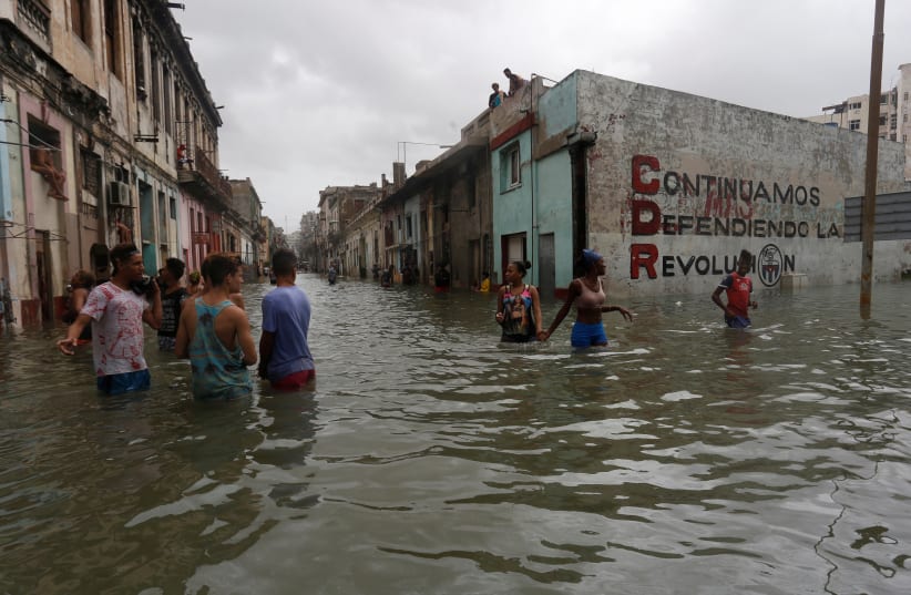 People wade through a flooded street, after the passing of Hurricane Irma, in Havana, Cuba. The sign on the wall reads "We will continue to defend the revolution. (photo credit: STRINGER/ REUTERS)