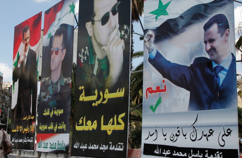 A woman walks past election posters of Syria’s President Bashar Assad along a street in Damascus in 2014. (photo credit: REUTERS)