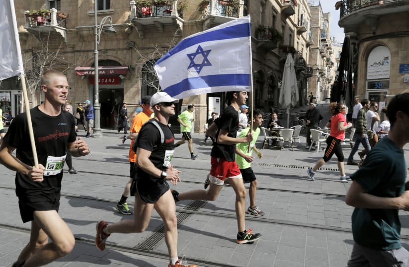 An athlete runs with an Israeli flag during the fifth international Jerusalem Marathon, March 13, 2015. (photo credit: REUTERS)