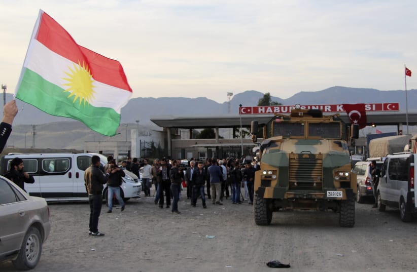 A man waves a Kurdistan flag as a Turkish military truck escorts a convoy of peshmerga vehicles at Habur border gate, which separates Turkey from Iraq, near the town of Silopi in southeastern Turkey. (photo credit: REUTERS)