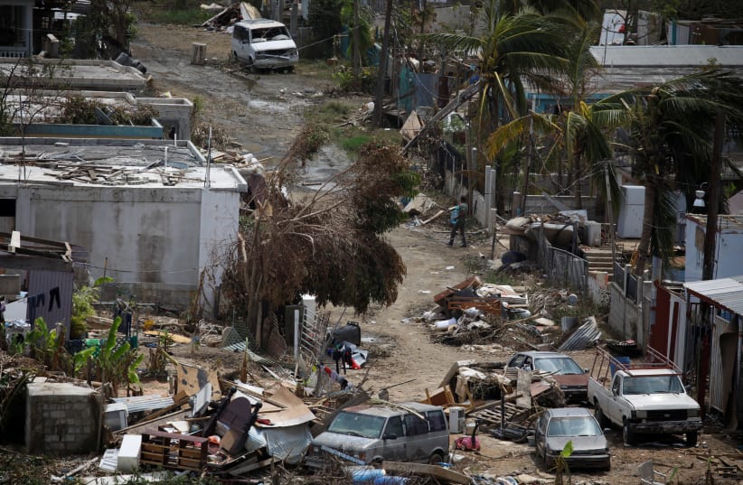 A man carrying a water container walks next to damaged houses after the area was hit by Hurricane Maria in Canovanas, Puerto Rico. (photo credit: CARLOS GARCIA RAWLINS/ REUTERS)