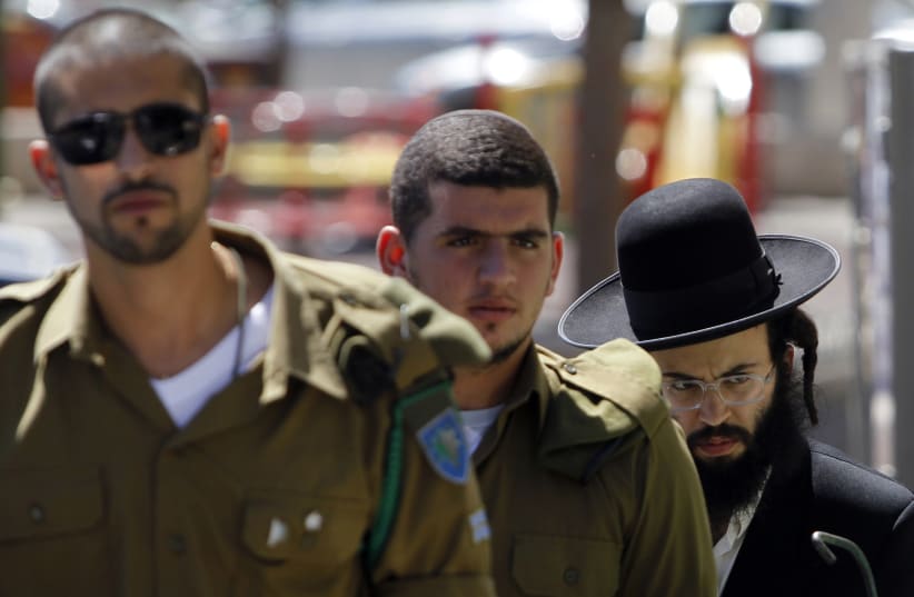 An ultra-Orthodox Jewish man walks behind Israeli soldiers at the entrance to a recruiting office in Jerusalem July 4, 2012.  (photo credit: REUTERS)
