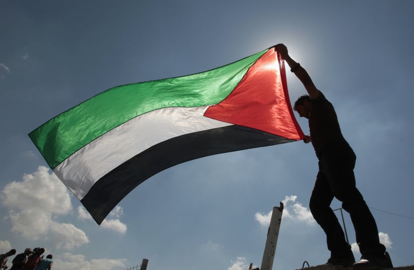 A Palestinian holds a flag during a protest (photo credit: REUTERS)