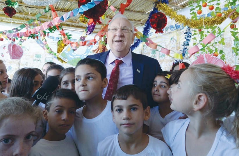 PRESIDENT REUVEN RIVLIN is joined by fourth-grade pupils from the Ariel mixed religious-secular school in the capital’s Gilo neighborhood, who are there to help him decorate the sukka at the President’s Residence. (photo credit: MARK NEYMAN/GPO)